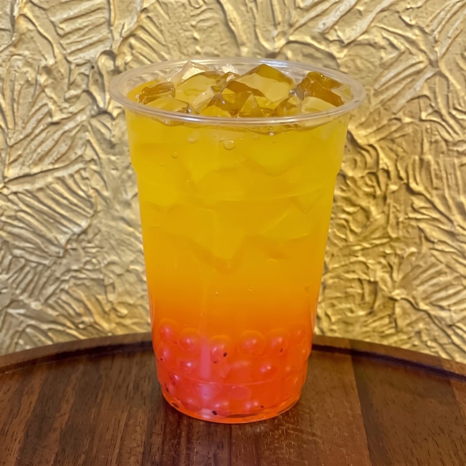 Bright orange-yellow layered beverage with ice in a clear plastic cup on a wooden table.
